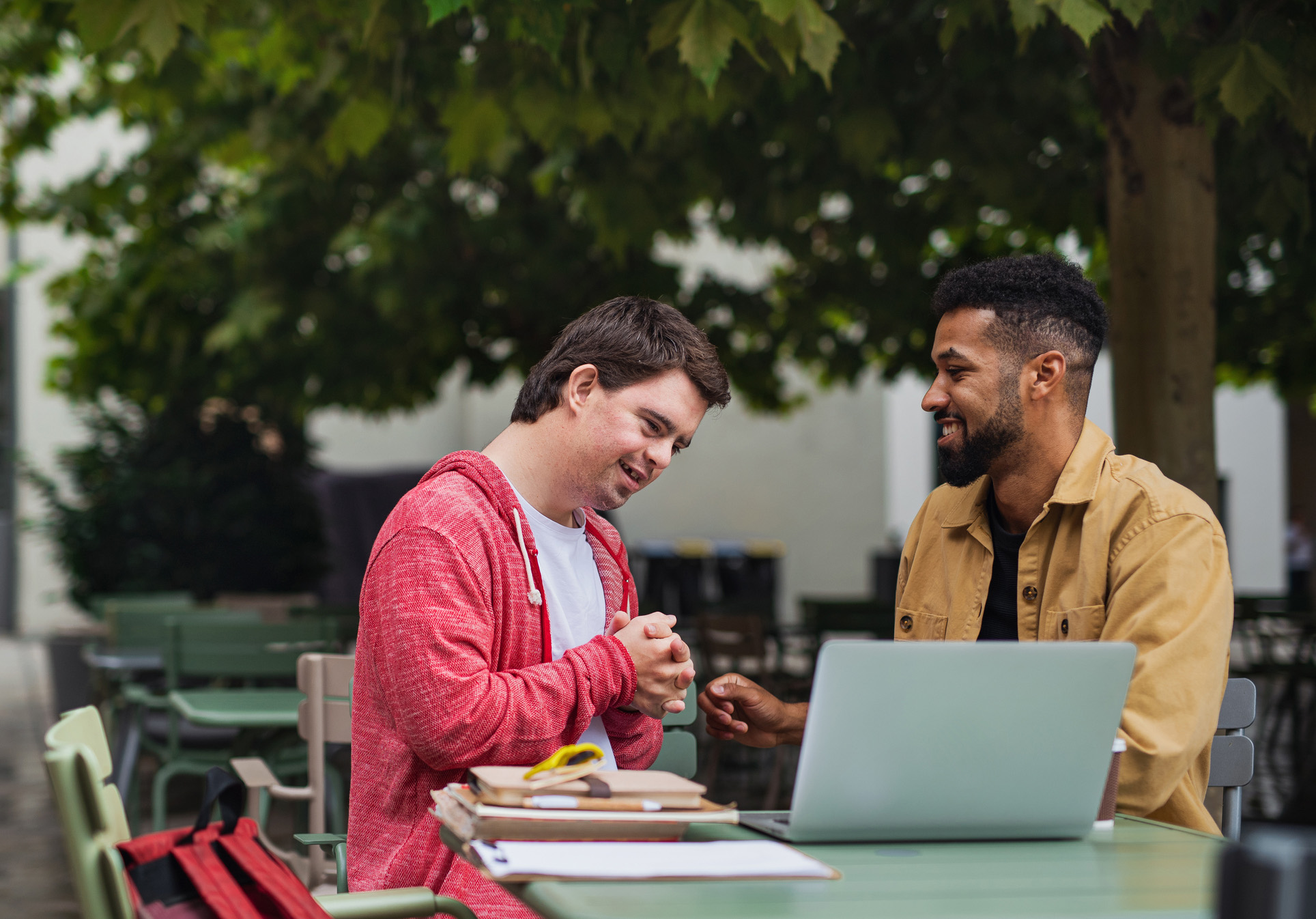 Twee mannen die lachend naar elkaar kijken bij een laptop.